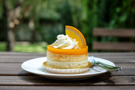 orange cake with orange topping and whipped cream in white dish on wooden topの写真素材