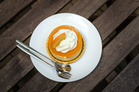 top view of orange cake with orange topping and whipped cream in white dish on wooden topの写真素材