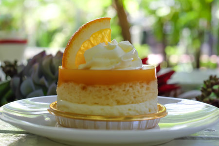 orange cake with orange topping and whipped cream in white dish on wooden topの写真素材