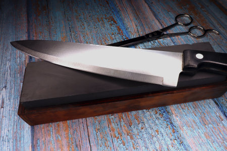 Steel blade on a sharpening stone against a faded wooden background
