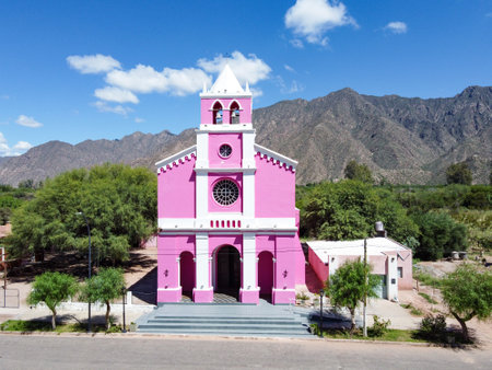 Majestic Church of Our Lady of Candelaria, Copacabana, Tinogasta. Its pink facade contrasts with the clear blue sky and imposing Catamarca mountains, an icon of the Adobe Route and Andean faith.の写真素材