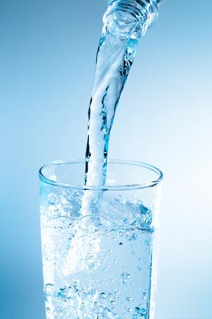 Pouring water from bottle into glass with blue lightの写真素材