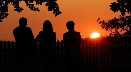 Silhouettes of a man and two women watching the sunsetの写真素材