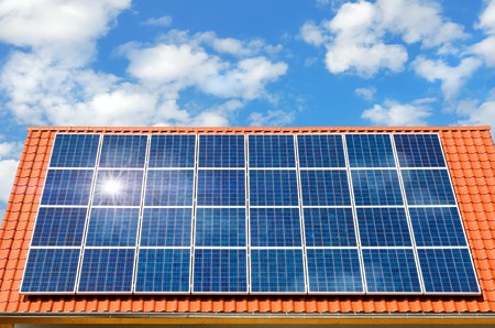 Roof with solar panel reflecting the sun, in the background a perfect sky with fluffy white cloudsの写真素材