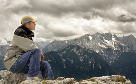 Young man sitting on a mountaintop and enjoying the majestic view