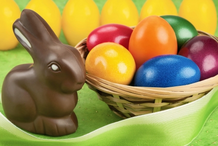 Chocolate Easter bunny and painted eggs in a basket, with light green and yellow backgroundの写真素材