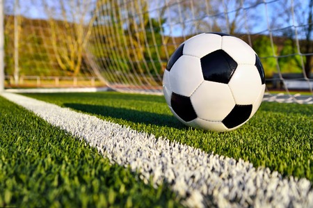Football lying on the green soccer pitch behind the goal line