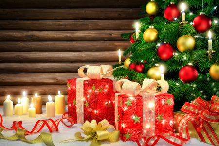 Shiny Christmas scene with a Christmas tree, candles, ornamental gift boxes with lamps, bows, snow and a rustic wooden wall backgroundの写真素材