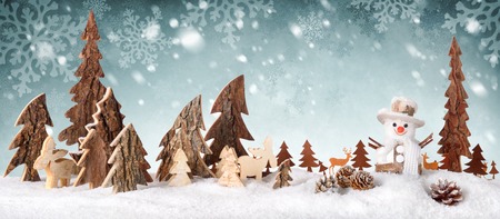 Wooden decoration arranged as a cute winter scene with a snowman, conifer trees, Christmas star, animals and snow, on a snowflakes backgroundの写真素材