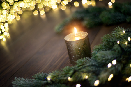 Christmas mood with candle, fir branches and lights on dark wooden tableの写真素材