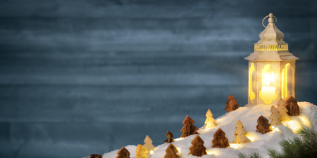 Christmas arrangement with wide wooden wall and carved ornamental trees on snow in the warm candlelight of a beautiful lanternの写真素材