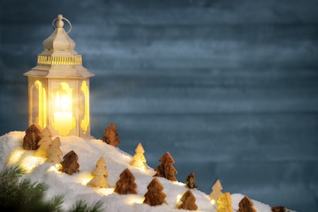 Christmas arrangement with blue wooden wall and carved ornamental trees on snow in the warm candlelight of a beautiful lanternの写真素材