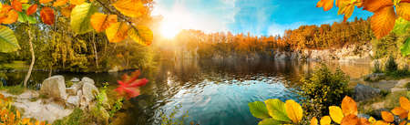 Magnificent autumn landscape panorama with colorful foliage framing a beautiful blue lake, with sun and blue skyの写真素材