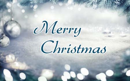 Christmas card with snow background and Merry Christmas lettering framed by fir branches, lights and ornamentsの写真素材