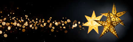Ornamental gold star lanterns for Christmas on black background with golden bokeh stardust, extra wide formatの写真素材