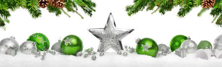 Christmas decoration with stars and baubles in silver and green, arranged on snow below hanging fir branches, symmetrical, isolated on white backgroundの写真素材