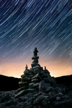 Night sky with star trails over stacked balanced stone arrangement, centered vertical compositionの写真素材