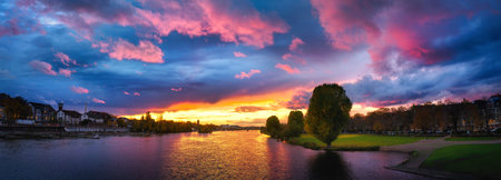 Spectacular sunset over Neckar river in Heidelberg, Germany. Colorful sky with pink and blue clouds and the golden sunlight reflected in the water at dusk, panoramic formatの写真素材