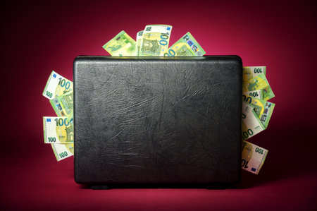 A briefcase overflowing with euro banknotes. Concept studio shot on illuminated burgundy red...