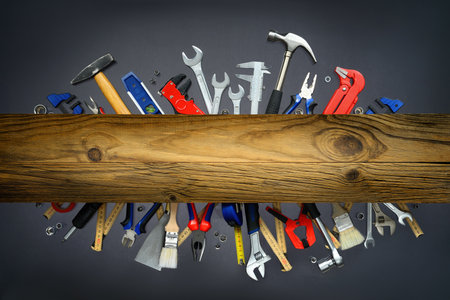 A set of tools on gray background with a wooden plank on top in an eye-catching arrangement. The elegant wood in the middle can be used as copy spaceの写真素材