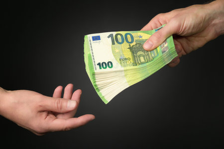 A man's hand receiving a heap of money from another, dark studio background. A symbolic concept shot for business and financial subjectsの写真素材