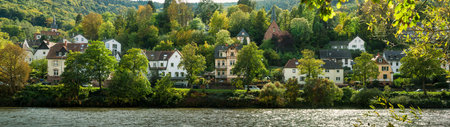 Scenic residential area at Neckar river in Heidelberg, Germany. Wide panorama shot with the river's water reflecting the sunlight in the foregroundの写真素材