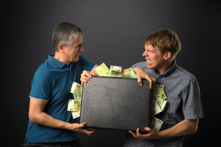 Finance concept shot with two angry people fighting over a suitcase full of money. Symbolizes greed,...