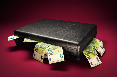 A briefcase overflowing with euro banknotes. Concept studio shot on illuminated burgundy red background with dark vignetteの写真素材