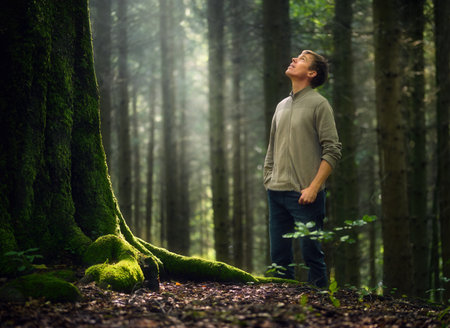 Hiker in forest looks up and marvels at a big tree. Environment and nature with a beautiful beam of sunlight.の写真素材