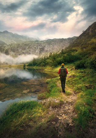 Hiker on a scenic footpath by a mountain lake. Beautiful hiking trail in the Alps with dramatic...