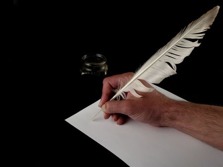 Hand holding a feather writing on white paper with ink (black background)の写真素材
