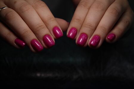 Closeup of hands of a young woman with dark red manicure on nails against white background