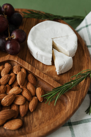 Camembert mold cheese, nuts, rosemary and grapes on a wooden round plate. Organic food. Stylish design, top view.の写真素材