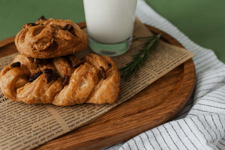 Baking with raisins and a glass of milk on a wooden plate on a green background. Homemade food. Stylish design.の写真素材