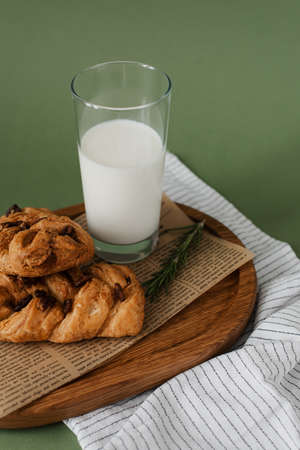 Useful breakfast on a wooden tray. Glass of milk and pastries with raisins on a green background. Stylish serving of food.の写真素材