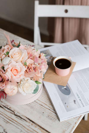 artificial flowers, a cup of coffee and an open magazine on a tableの写真素材