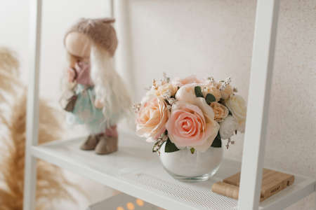 Delicate bouquet of pink flowers in a round vase on a white shelf. Beautiful decor for the home.の写真素材