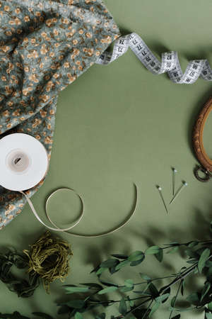 Objects for sewing on a green background flat lay. Hoops, measuring tape, thread, needles, decor, fabric top view.の写真素材