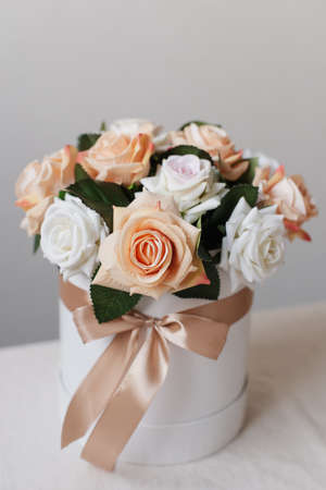 Artificial roses in a round box on a white table. Decorative bouquet of beautiful flowers.の写真素材