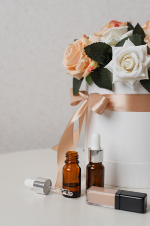 Tube of cosmetics next to beautiful flowers in a round box on a table.の写真素材