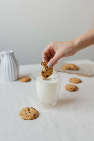 Female hand dipping cookies in milk. ... Glass glass with milk and cookies. A delicious and healthy breakfast.の写真素材