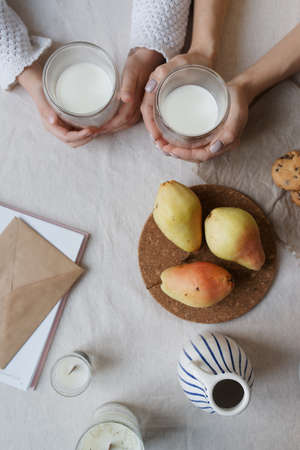 Glasses of milk in the hands of mother and child flat lay. Milk and fruit on the table as seen from...