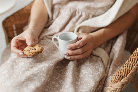 A woman is holding a white cup of coffee and an oatmeal cookie.の写真素材
