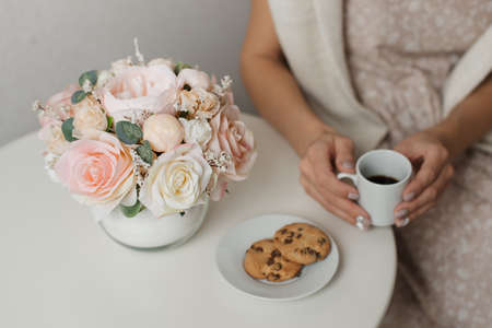 A woman drinks an Americano at a round table next to a bouquet of flowers. Beautiful flowers in a round vase.の写真素材