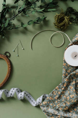 Items for sewing on a green background flat lay. Holes, measuring tape, thread, fabric top view.の写真素材