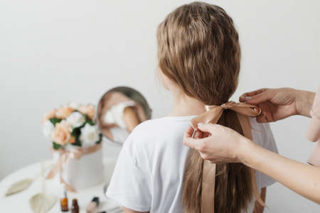 A mother does her daughter's hair by braiding her hair. A beautiful hairstyle for her little daughter.の写真素材