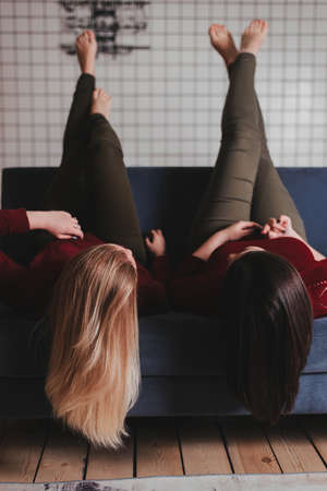 two girls lie on the couch upside down. Blue sofa