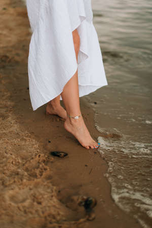 barefoot girl on the shore, a girl in a white dress walks along the shore. Summerの写真素材