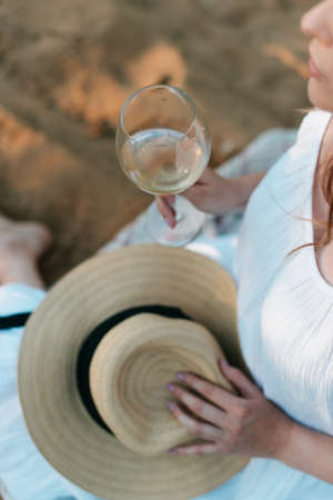 a girl in a white dress holds a straw hat and a glass of wine in her hands. Summer photo sessionの写真素材