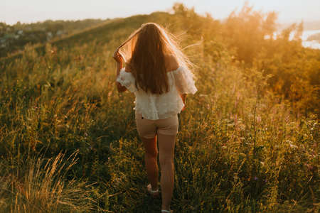 girl walks on a green field in the rays of the bright sun. Summer photo sessionの写真素材